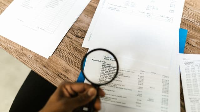A hand reviewing a printed document through a magnifying glass.