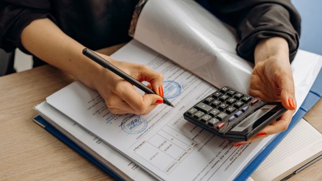 A person checking stamped paperwork with a pen and a calculator.